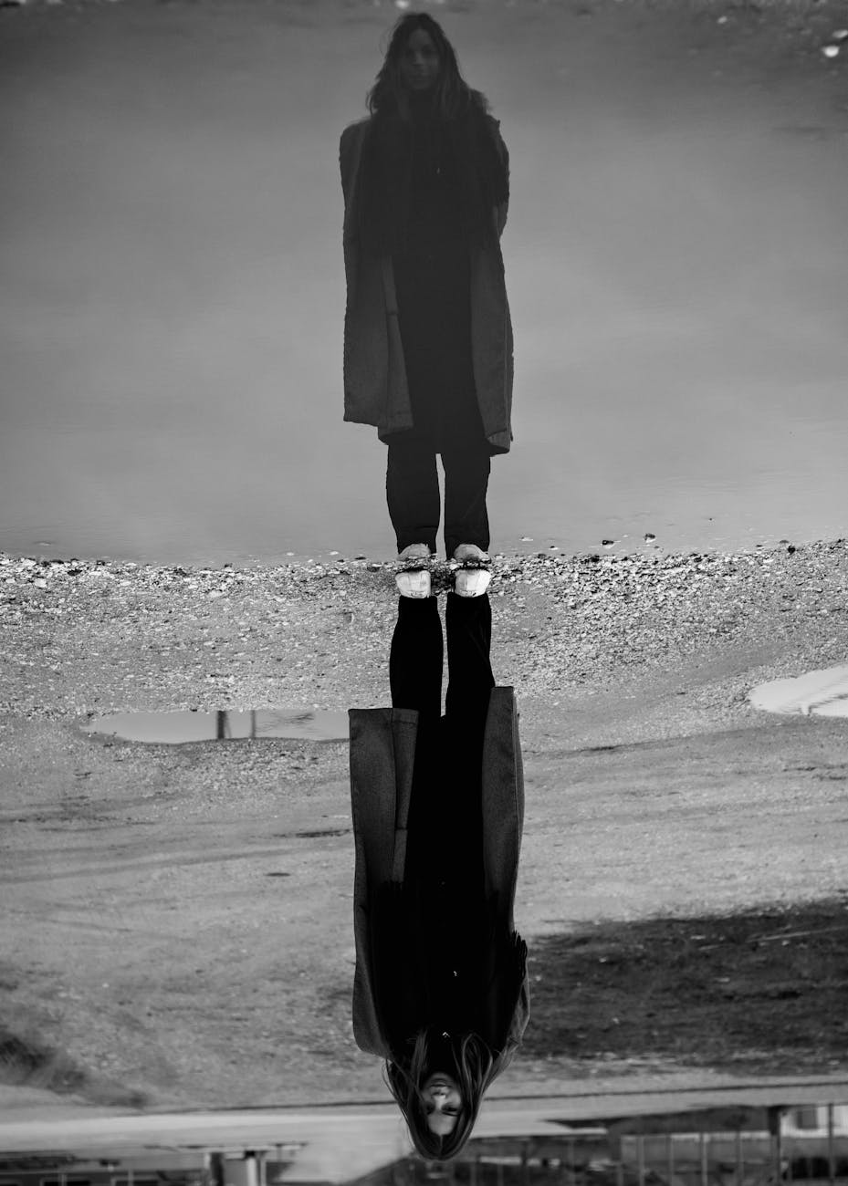 a grayscale photo of a reflection of a woman on water