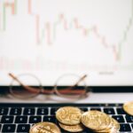 bitcoins lying on the laptop keyboard and a chart on the monitor