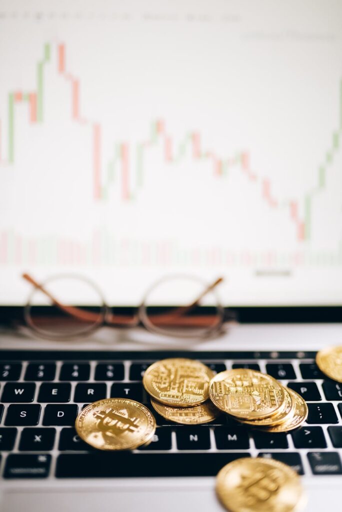 bitcoins lying on the laptop keyboard and a chart on the monitor