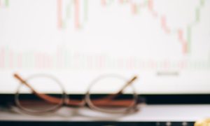bitcoins lying on the laptop keyboard and a chart on the monitor